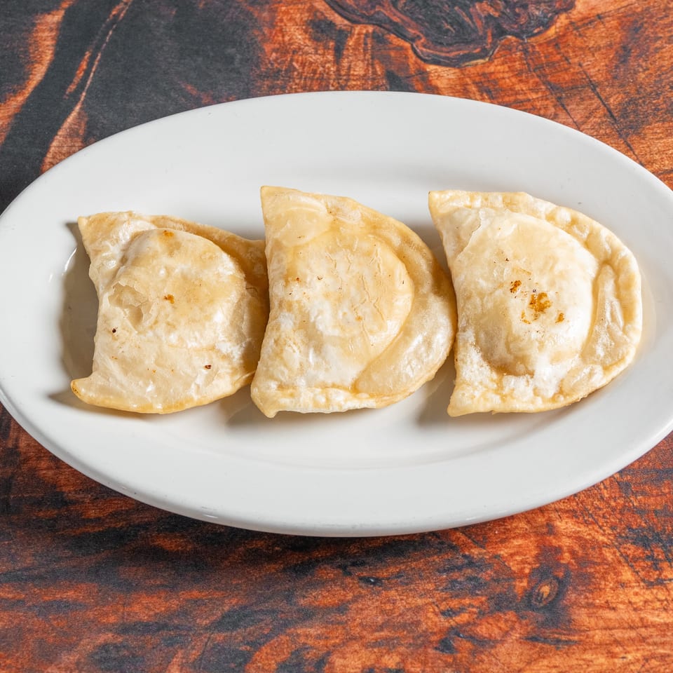 Three golden-brown pierogi, lightly fried, arranged on a white oval plate against a rustic wooden background.