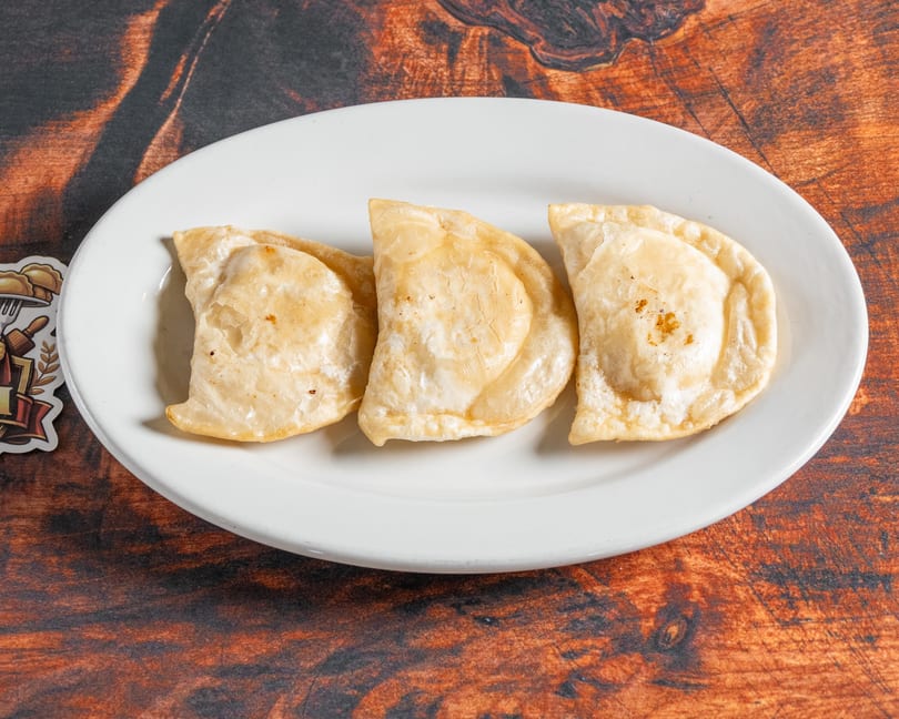 Three golden-brown pierogi, lightly fried, arranged on a white oval plate against a rustic wooden background.