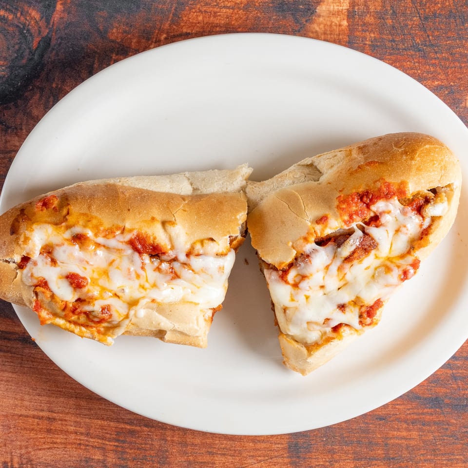 Two halves of a cheesy meatball sub sandwich with marinara sauce on a white plate.