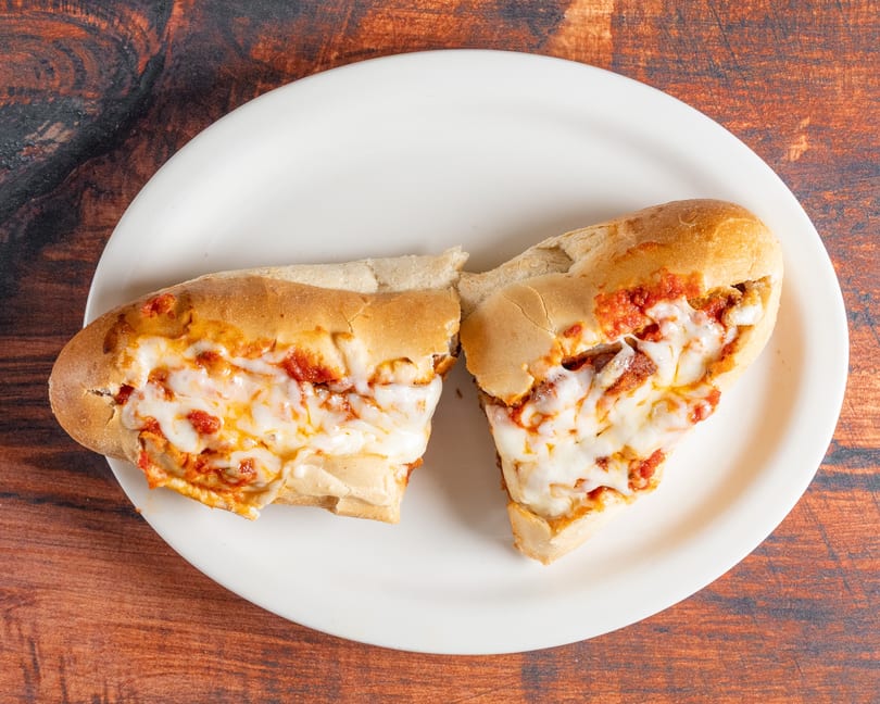 Two halves of a meatball sub sandwich, topped with melted mozzarella cheese and marinara sauce.
