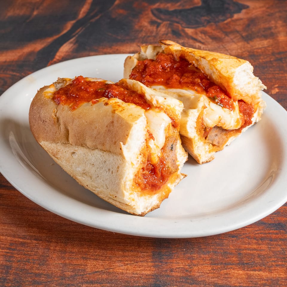 Two halves of a meatball sub sandwich with melted cheese and red sauce on a white plate.