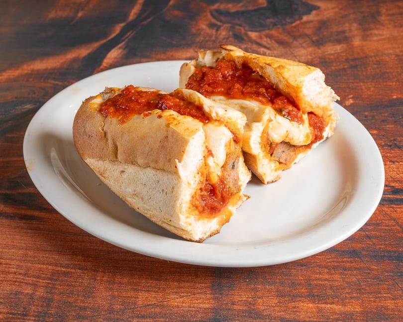 Two halves of a meatball sub sandwich with melted cheese and red sauce on a white plate.