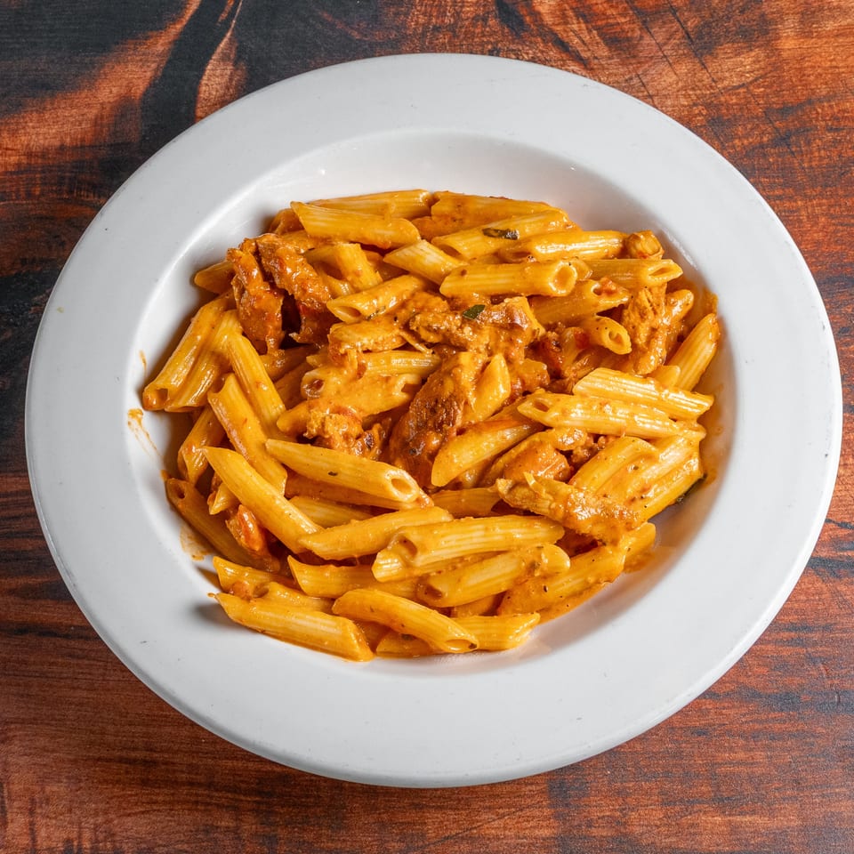 Penne pasta with chicken and creamy tomato sauce in a white bowl on a wooden table.