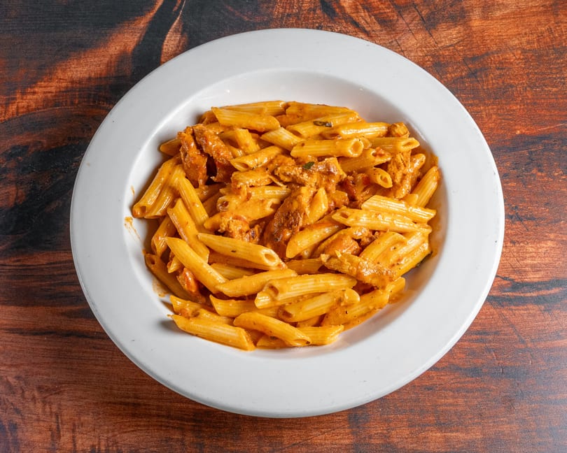 Penne pasta with chicken and creamy tomato sauce in a white bowl on a wooden table.