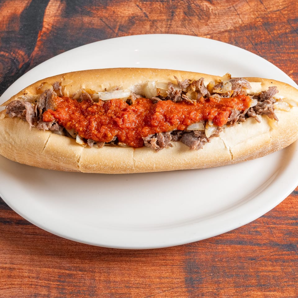 A cheesesteak hoagie with steak, onions, and red sauce on a white plate.
