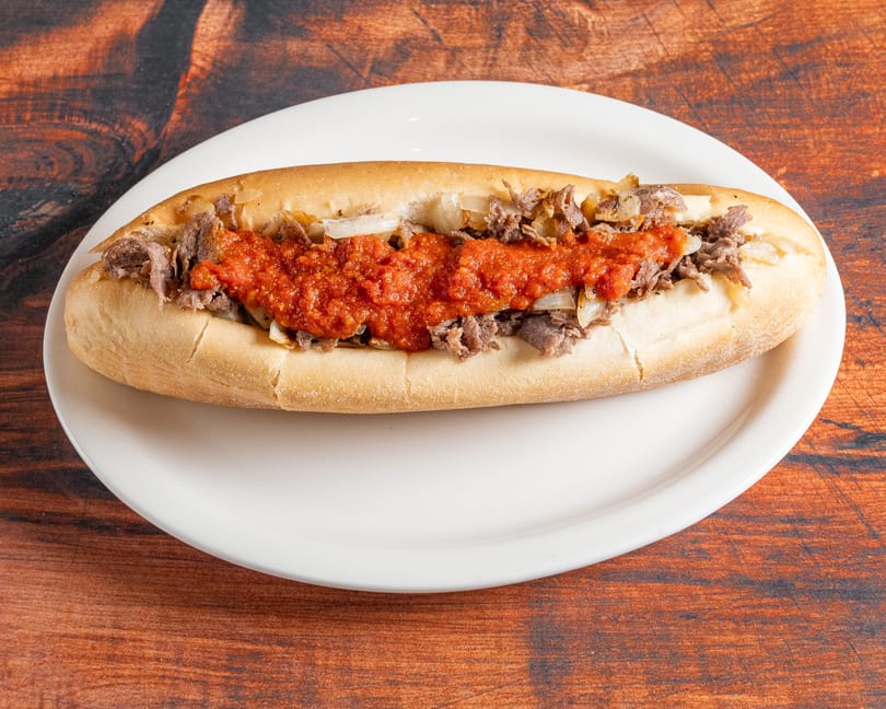 A cheesesteak hoagie with steak, onions, and red sauce on a white plate.