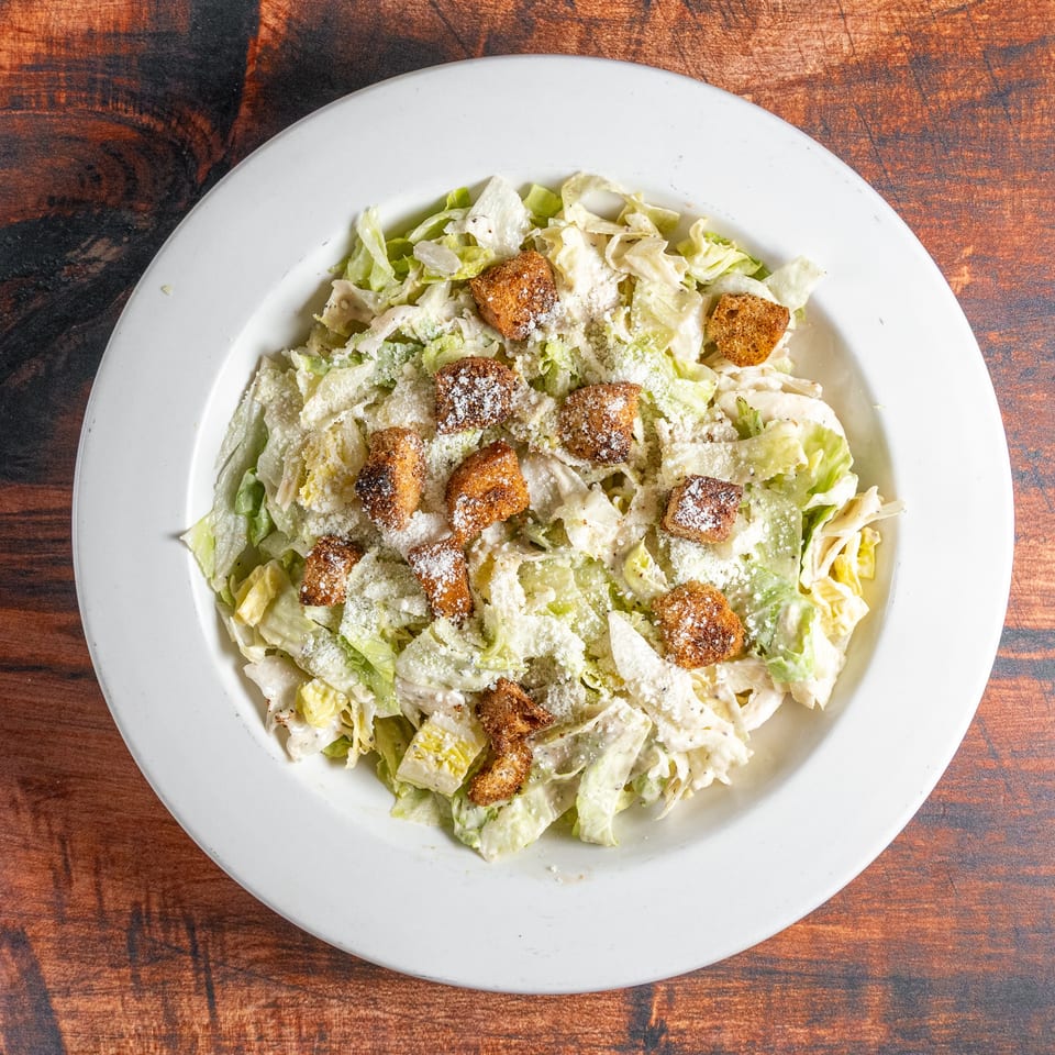 Overhead view of a Caesar salad with lettuce, croutons, and parmesan cheese in a white bowl.