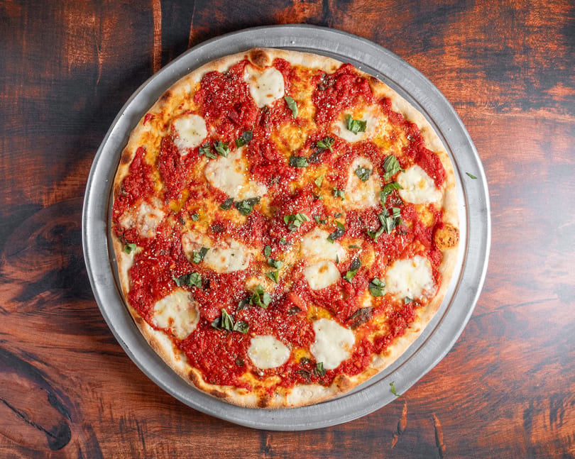 A freshly baked Margherita pizza with rich red sauce, mozzarella, and basil on a metal tray.