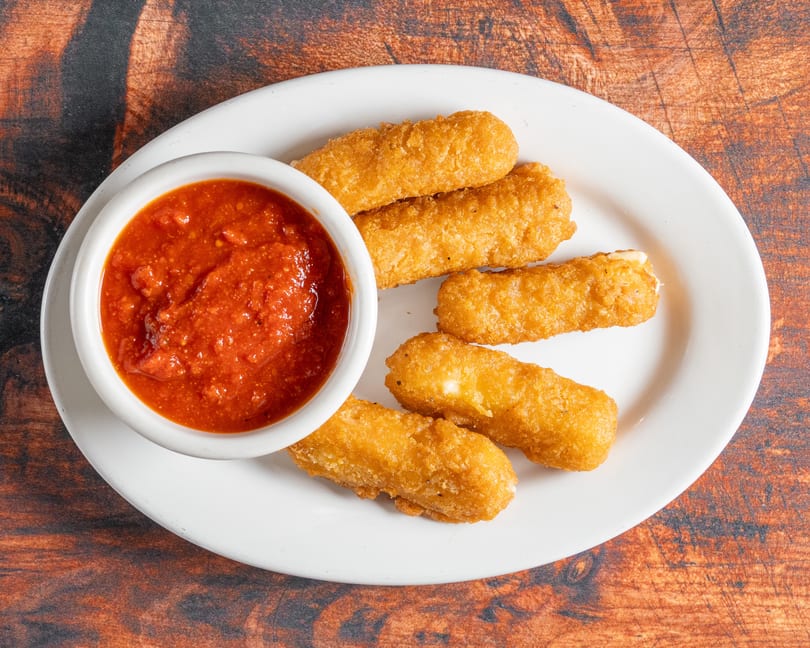 Golden-brown mozzarella sticks with a side of chunky red marinara sauce on a white plate.