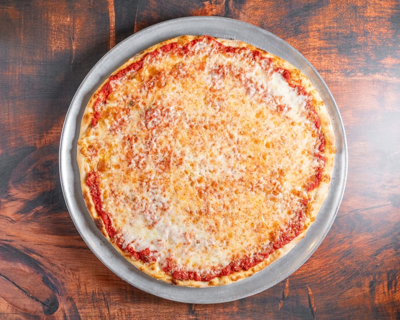 A classic cheese pizza with red sauce and melted mozzarella on a metal pan, on a wooden table.