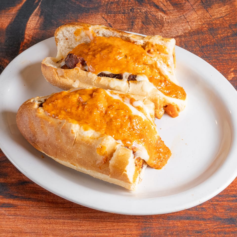 Two open-faced sandwiches with melted cheese and orange sauce on a white plate.