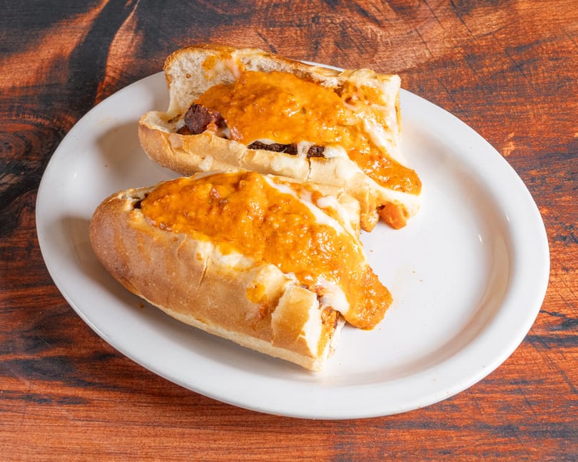 Two open-faced sandwiches with melted cheese and orange sauce on a white plate.