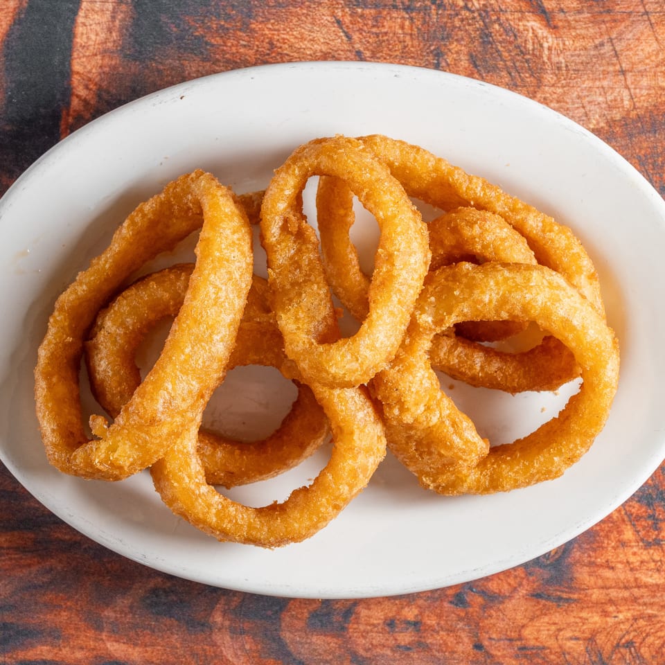 A white oval plate filled with golden-brown, crispy onion rings on a rustic wooden table.