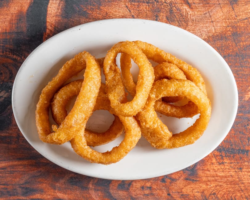 A white oval plate filled with golden-brown, crispy onion rings on a rustic wooden table.